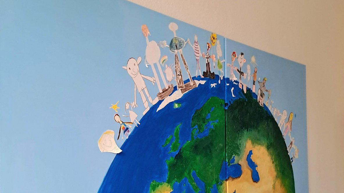 Wandbild einer Weltkugel mit unterschiedlichen Figuren darauf stehend