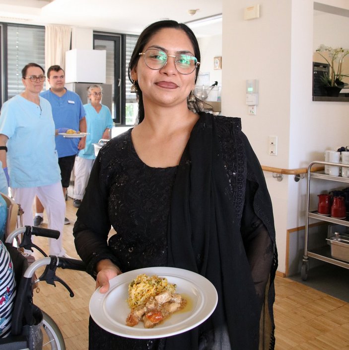 Eine Frau hält einen gefüllten Teller mit Essen und trägt traditionelle pakistanische Kleidung