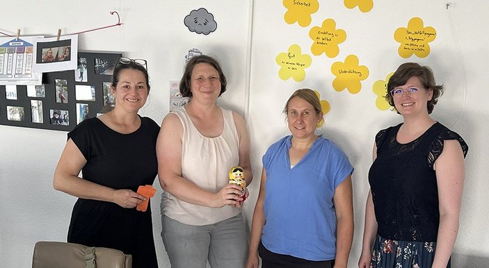 Vier Frauen lächeln in die Kamera und stehen vor einem Whiteboard mit Notizen