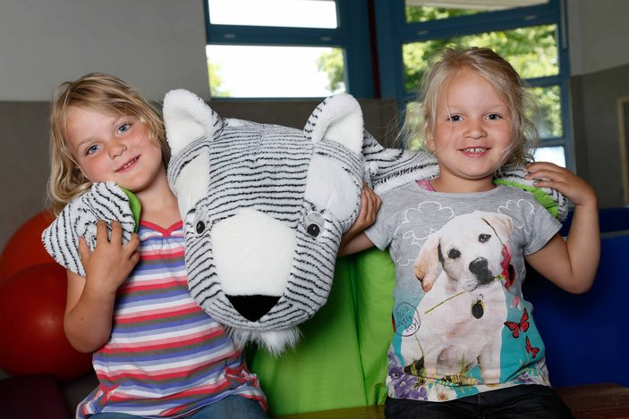 Zwei Mädchen lächeln in die Kamera und halten ein großes Kuscheltier