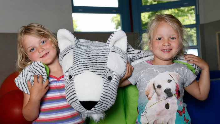 Zwei Mädchen lächeln in die Kamera und halten ein großes Kuscheltier