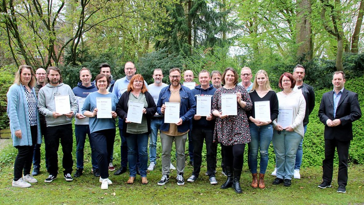 Ein Gruppenbild mit vielen Personen draußen, die ein Zertifikat in der Hand halten