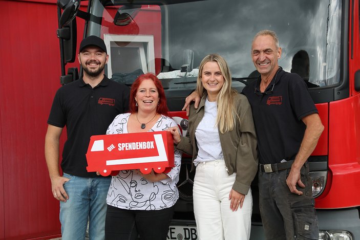 Die Geschäftsführung übergibt eine Spendenbox an die Mitarbeiterin der Wohngruppen, im Hintergrund ein Umzugs-LKW