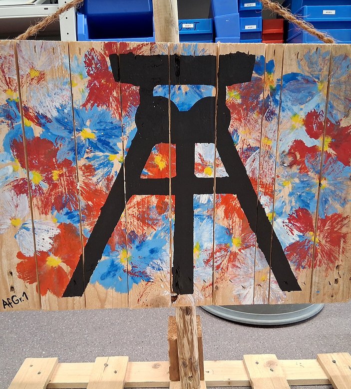 Kunstobjekt, welches aus Holz als Leinwand besteht und darauf ein Förderturm und eine Blumenwiese gemalt wurde.