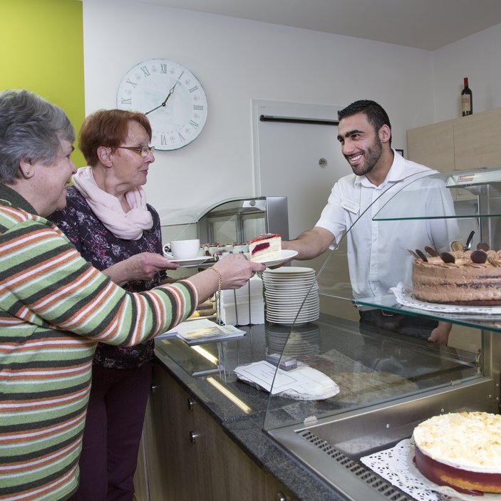 Mann reicht zwei Damen Kuchen in einem Café