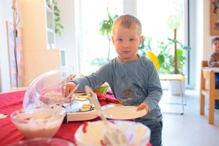 Junge steht an einem Frühstücksbuffet und schaut in Kamera
