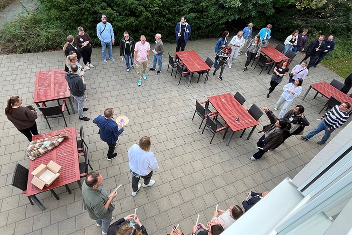 Blick aus der ersten Etage auf die Diakonie-Terrasse, wo sich die Teilnehmenden zu einer kurzen Andacht im Halbkreis versammelt haben