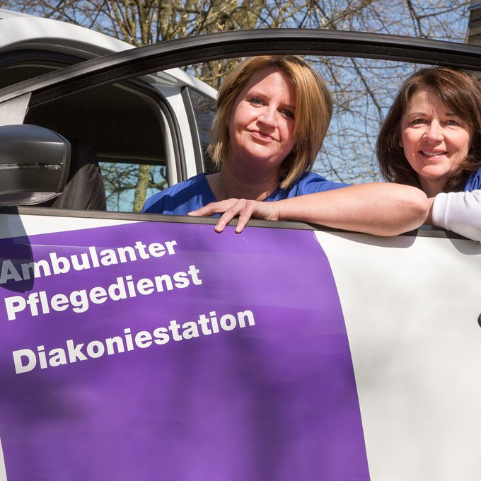 Zwei Frauen lehnen an einer Autotür der Diakoniestation und lächeln