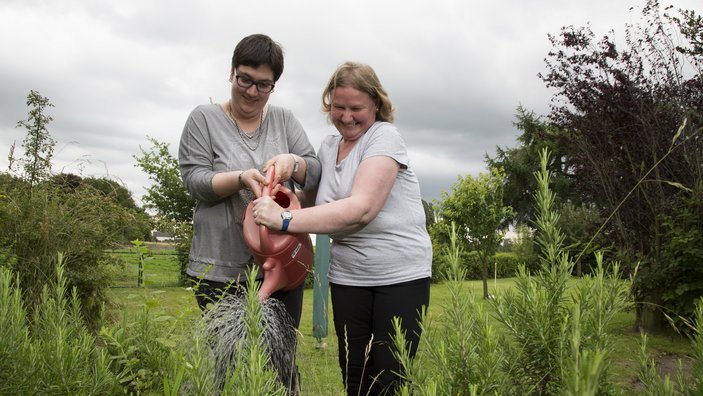 Zwei Frauen gießen gemeinsam den Garten