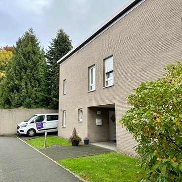Außenansicht des Wohnhauses mit Flachdach, daneben ein Diakonie-Auto