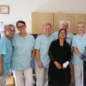 das Küchenteam posiert am Essens-Ausgabe-Wagen und lächelt in die Kamera