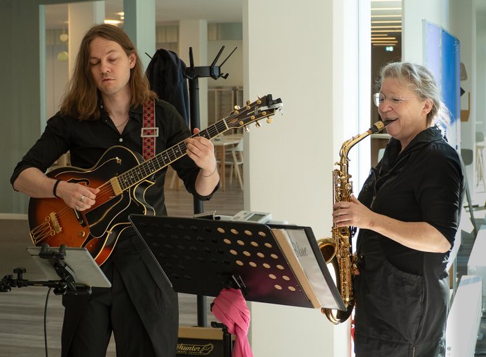 links ein Musiker an der E-Gitarre, rechts eine Saxophonistin