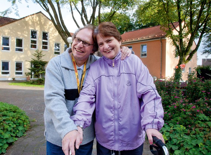 Zwei Personen lächeln in die Kamera, hinter den beiden sieht man einen Wohnkomplex