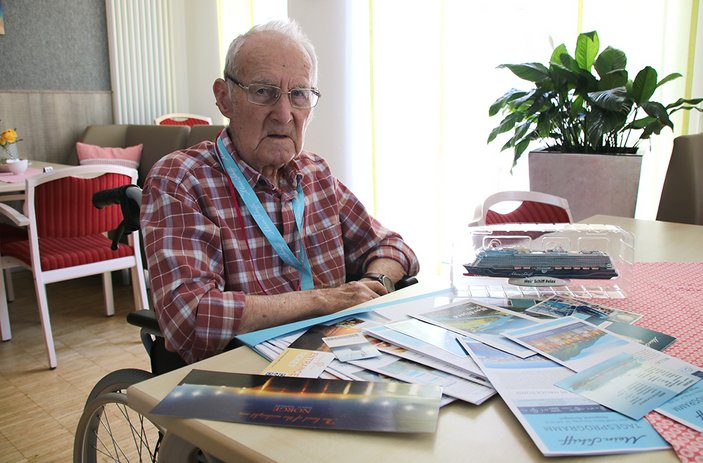 Älterer Herr im karierten Hemd, im Rollstuhl sitzend, vor sich ausgebreitet die Reiseunterlagen