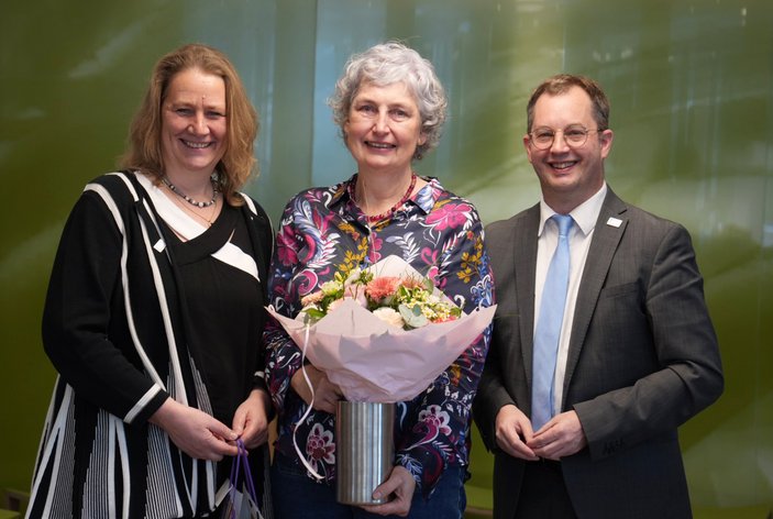 Die Neu-Ruheständlerin mit der Geschäftsführung vor der grünen Glaswand 