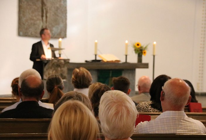 Die Köpfe von Kirchenbesuchern von hinten, im Hintergrund Dr. Kehlbreier am Rednerpult