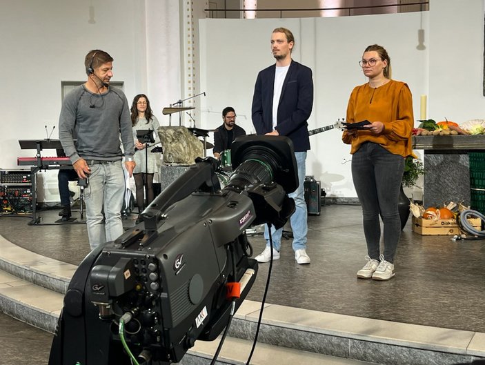 Vorne eine TV-Kamera, im HIntergrund gibt der Aufnahmeleiter letzte Anweisungen an das Team